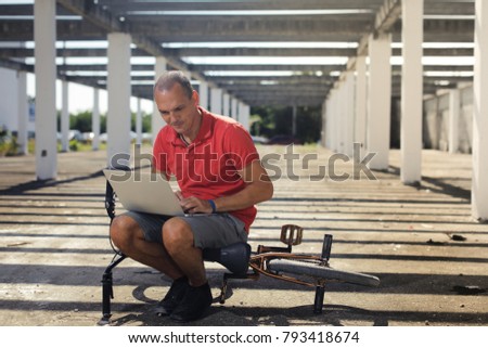 BMX rider on the bike looking at notebook on the street indoors the not ready building with striped shade from the sun