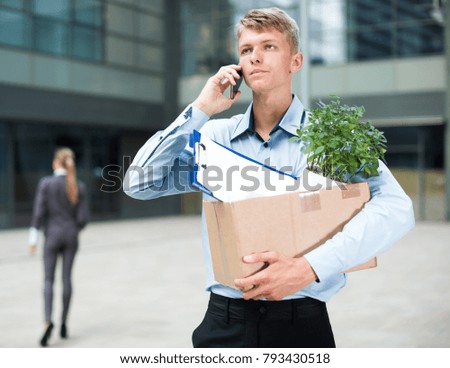 Young businessman with box is talking phone and searching new job outdoor.