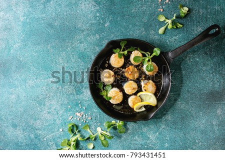 Fried scallops with butter lemon spicy sauce in cast-iron pan served with green salad over turquoise texture background. Top view, copy space Royalty-Free Stock Photo #793431451