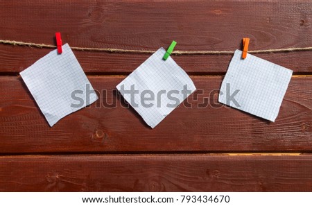 Three white sheets for notes hanging on the rope with clothespin on the wooden wall. Mock up for design.