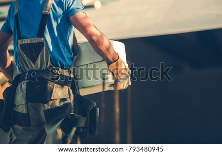 Construction Site Contractor Moving Heavy Building Materials in His Hands. Residential Development Industry. Royalty-Free Stock Photo #793480945