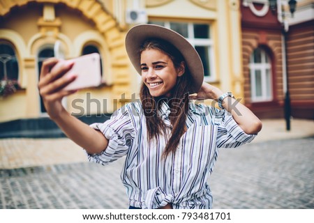 Cheerful female tourist making photo on front smartphone camera walking in architectural modern city.Happy traveller shooting video for personal blog using phone and 4G internet connection in roaming
