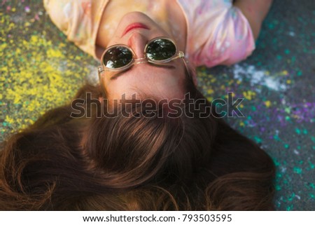 Closeup portrait of lovely young model in mirror glasses lying on the asphalt covered powder Holi