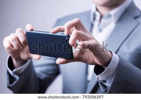 Closeup of a businessman in grey suit taking picture with a mobile phone