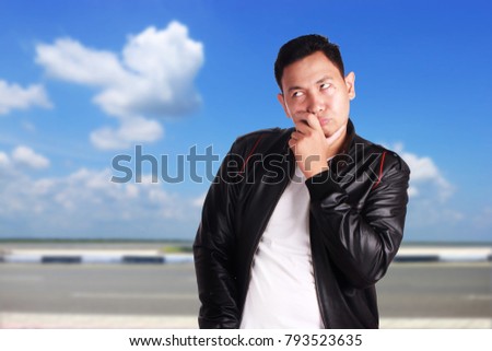 Attractive young Asian man wearing black leather jacket thinking gesture, over cloudy blue sky background