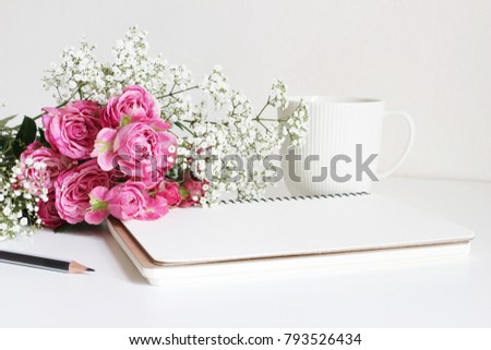 Wedding styled stock photo. Still life with pink roses, baby's breath Gypsophila flowers, white cup, pencil and notebook. Floral composition. Image for blog or social media.