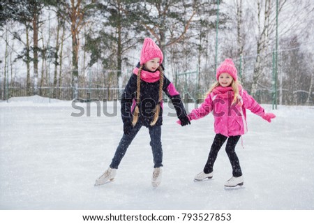 Two Little smiling girls skating on ice in pink wear. Outdoor