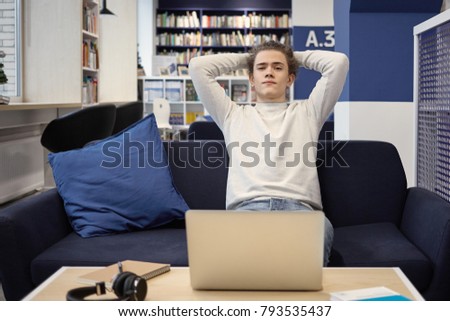 People, rest, leisure and relaxation concept. Picture of modern stylish young man relaxing at home using electronic device and headset, keeping hands behind his head, his look expressing carefreeness