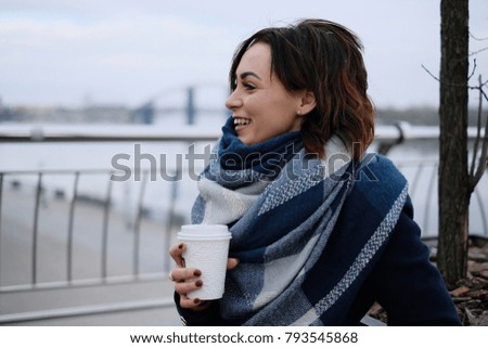 Portrait of attractive young woman with dark hair wearing scarf and holding white coffee cup on a cold and snowy winter day
