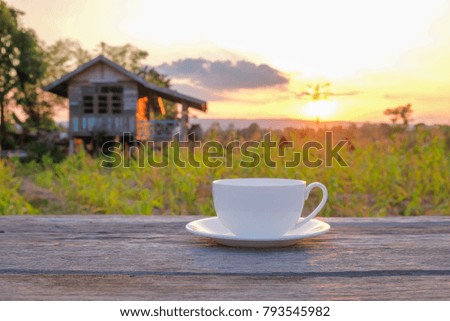 a front selective focus picture of a cup of coffee on wooden table beside agriculture field. 