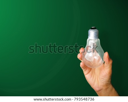 Men's hand holding a light bulb on green background.