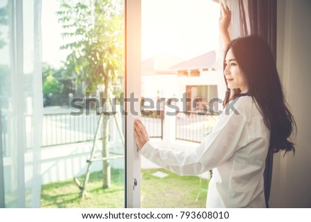 Asian girl who just wake up in the morning as relaxed. She's read one book on the bed. She opened the window to receive the light of the morning sun. She was holding a glass of coffee to drink it.