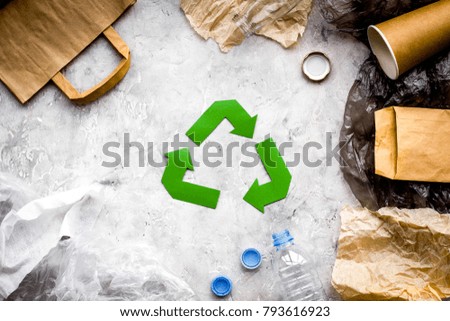 Eco-friendly life. Green paper recycling sign among waste paper, plastic, polyethylene on grey background top view