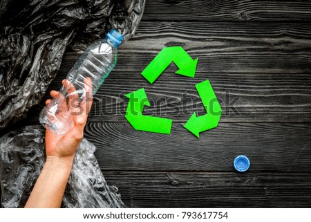 Recycle plastic and polyethylene waste. Botlles and bags near green recycle sign on grey wooden background top view copy space