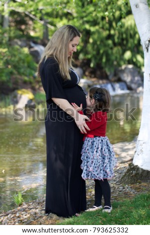Enjoying Pregnancy, expecting maternity, maternity photography, beautiful young  Mother with Daughter outside, Kissing Mothers Belly, warm sunny picture Waterfall Background , Happy Family Concept