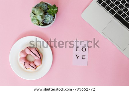 on a pink paper background lie a laptop, a donut in pink glaze, card with the inscription "Love", a flower succulent