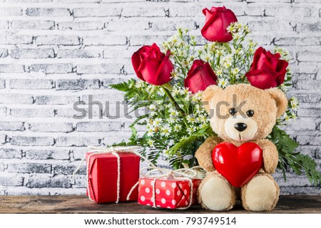 A photo of Teddy bear holding a heart-shaped balloon with red gift box and white brick wall background, Valentine concept