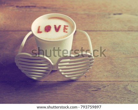 Valentine's day concept coffee cups with “LOVE” on frothy surface, wooden background with blurred plastic heart-shaped glasses. (selective focus, vintage filter)