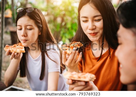 Asian students eating eating the pizza together in breaking time early next study class having fun and enjoy party, Italian food slice with cheese delicious at university outdoor. Royalty-Free Stock Photo #793769323