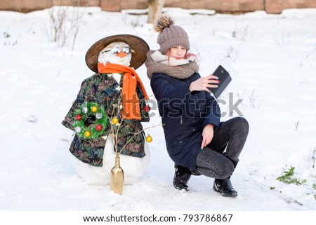 Happy young girl is taking pictures of selfie with a snowman, close up