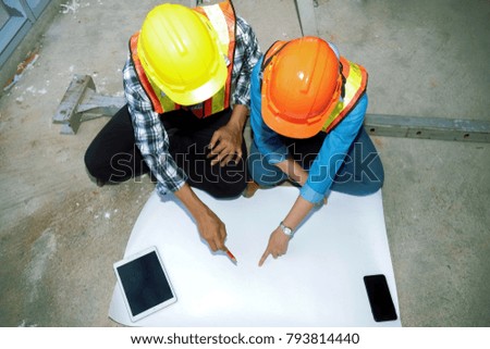 Architects in the construction site :  Top view, two male and female architects sit on the floor in the workplace, put together a blueprint. Selective Focus 