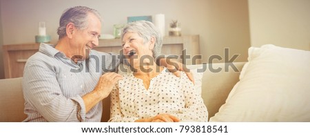 Romantic senior couple laughing while sitting on sofa at home Royalty-Free Stock Photo #793818541