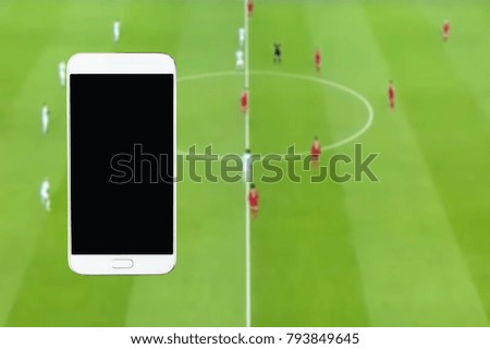 Mobile phone, blur image of football match from the television screen as  background.