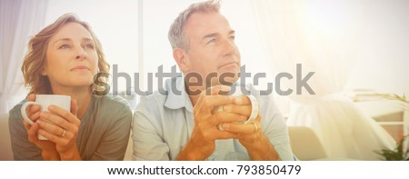 Thoughtful middle aged couple sitting on the couch having coffee looking away at home in the living room Royalty-Free Stock Photo #793850479