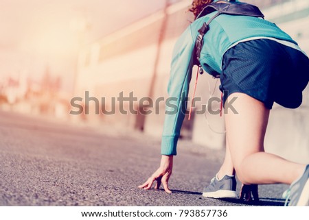 Young fit woman with running backpack in start pose preparing for rush in industrial urban area