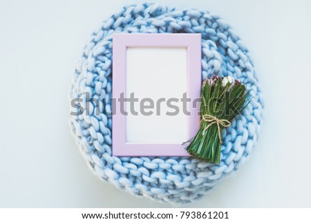 Pink photo frame mock up with space for text in the center of woolen plaid knit and bouquet of spring flowers on a white background. Flat lay, top view.