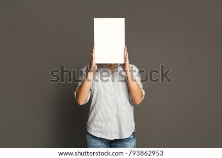 Young woman with blank white paper at face. Serious girl covering her head with advertising sheet, copy space