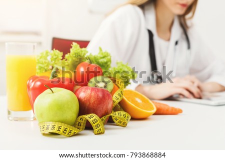 Nutritionist desk with healthy fruit, juice and measuring tape. Dietitian working on diet plan. Weight loss and right nutrition concept Royalty-Free Stock Photo #793868884