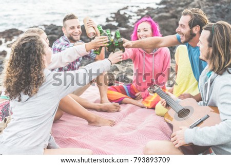 Happy friends cheering with beers and playing music in camping outdoor - Trendy people having fun together doing pic-nic - Friendship, youth lifestyle and vacation concept - Focus on hands bottles