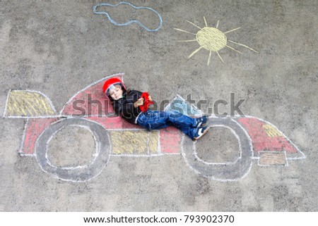 Adorable little kid boy drawing with colorful chalks race car picture on asphalt. Cute toddler and preschool child playing racing driver. Creative leisure with small kids outdoors