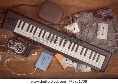 90's vintage musician lifestyle accessories concept with keyboard instrument,old medium format camera,loudspeaker,compact cassettes,jeans,portable cassette player and sunglasses ,vintage filter.
