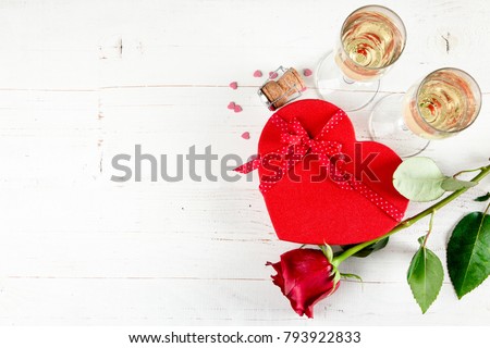 Background of Valentines day celebration with champagne, roses, heart shaped present and red candies on a white wooden background.