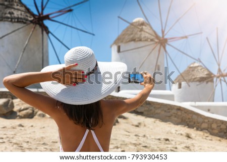 Tourist woman with white hat takes a picture of the famous windmills of Mykonos, Greece