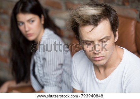 Young sad cheated man thinking of betrayal unresolved problem in bad relationship, upset girlfriend at background, depressed husband sitting his back to frustrated wife, unhappy couple after quarrel Royalty-Free Stock Photo #793940848