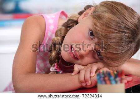 little girl with crayons resting head on desk