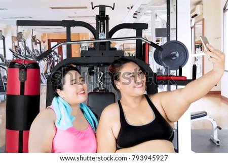 Two obese women taking a selfie photo with a smartphone after workout in the gym center