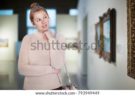 Portrait of young woman standing near the painting in baguette at the art museum 