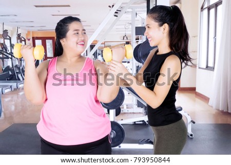 Picture of female trainer helping a fat woman to exercising with dumbbells in the fitness center