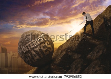 Picture of European businessman pulling a rock with text of interest rates while climbing on the cliff