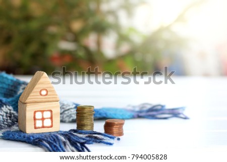 wooden house with a warm scarf next to a pile of coins / inexpensive cozy accommodation