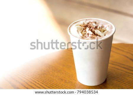 Hot chocolate with whipping cream in white paper cup on wooden table background with copy space.