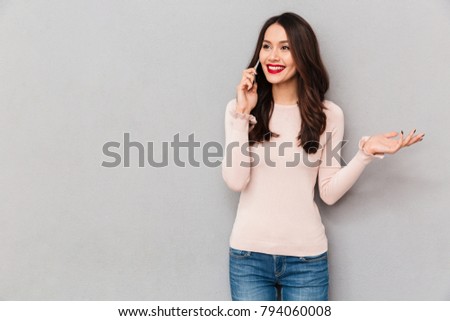 Portrait of adorable smiling woman with trendy hair talking on mobile phone having pleasant conversation, over gray background