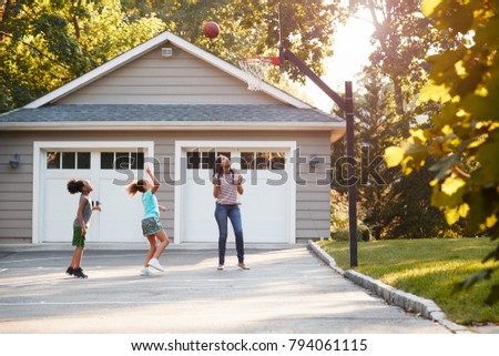Mother And Children Playing Basketball On Driveway At Home