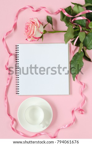 Pink blooming fresh rose flower with cup for coffee and notebook on pink background. Copy space composition. Overhead shots