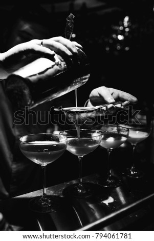 black and white close photograph bartender hands, which makes and pours cocktail from shaker into glass