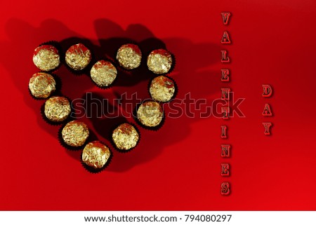Postcard on Valentine's day. On a red background are candy in a Golden wrapper . They are laid out in the shape of a heart .